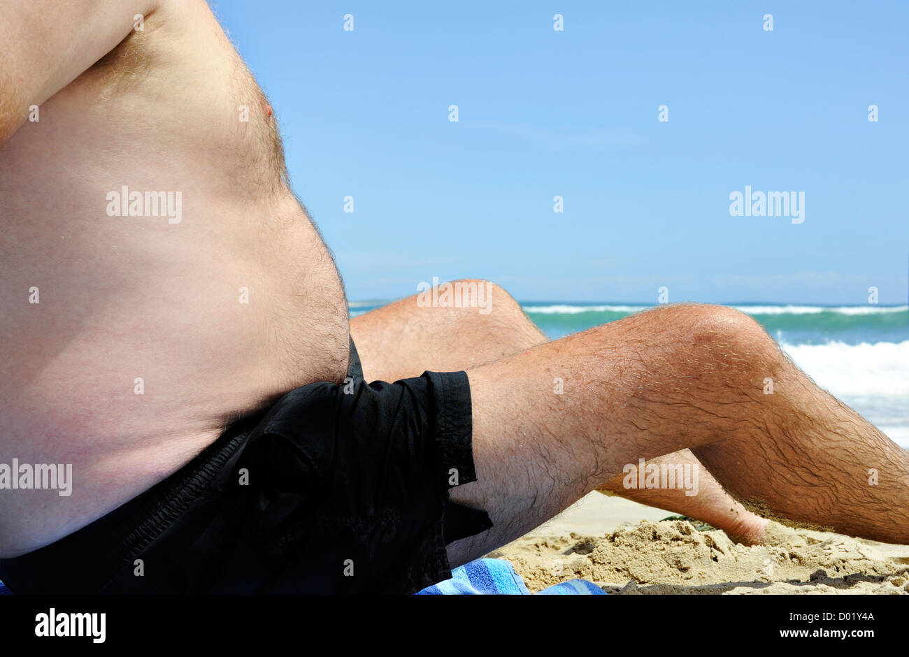 Grasso malsano uomo seduto sulla spiaggia in una giornata di sole Foto Stock