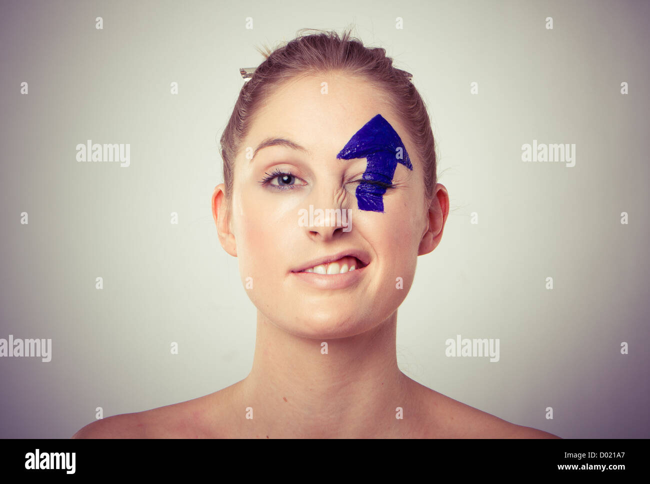 Ritratto di giovane sorridente dai capelli biondi donna con verso l'alto freccia dipinta over eye, bianco di sfondo per studio. Foto Stock