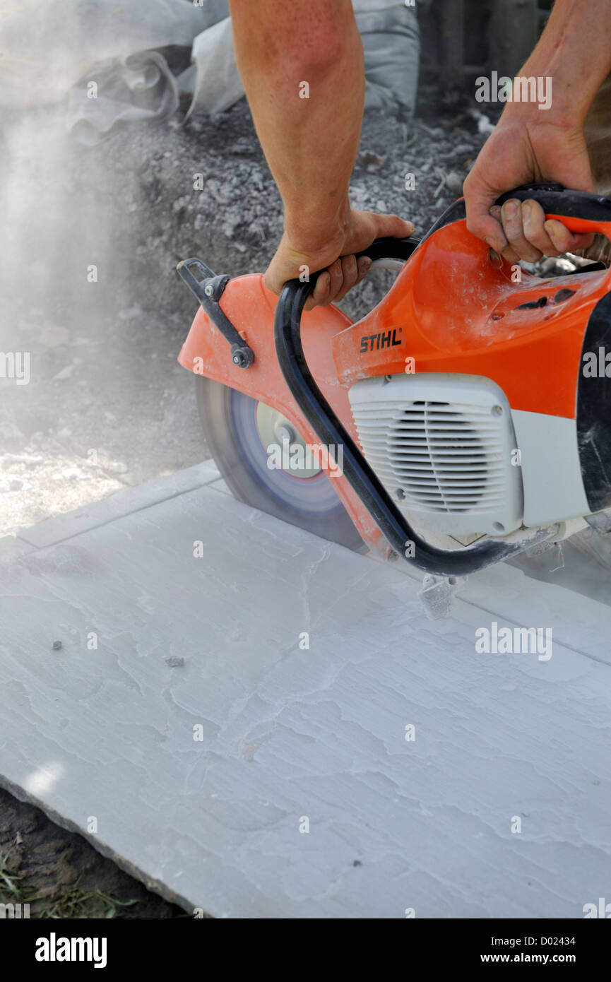 Builder utilizzando un taglio a secco di pietra portatile sega per tagliare una lastra di pavimentazione Foto Stock