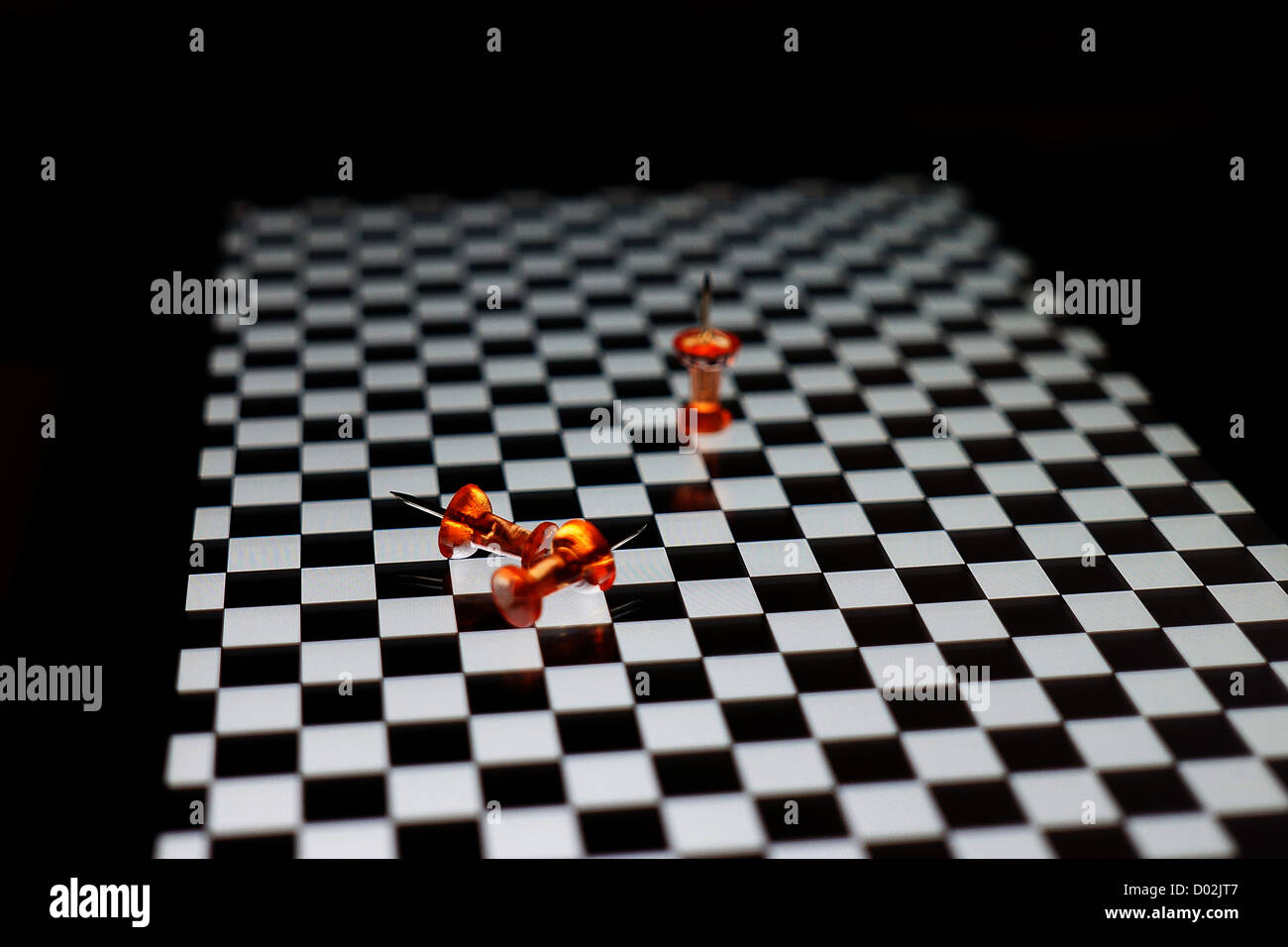 Orange puntine da disegno sulla superficie a scacchi Foto Stock
