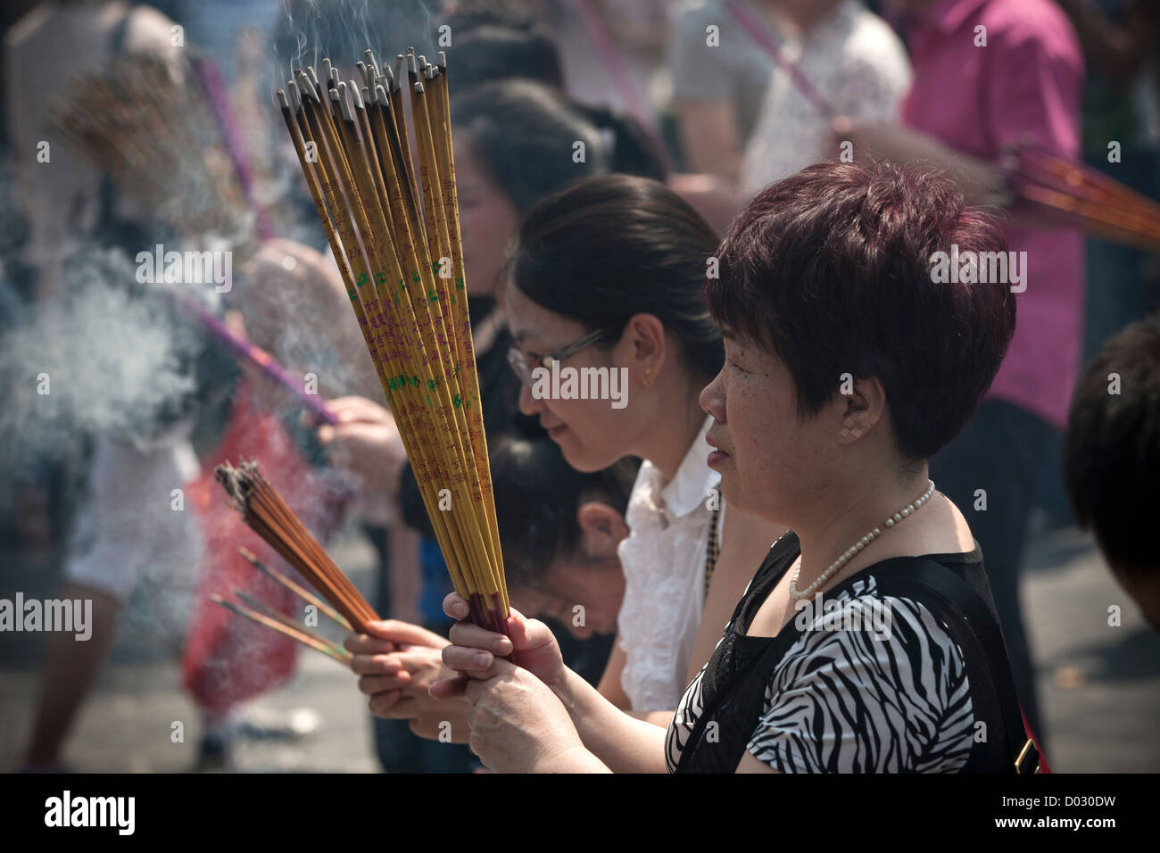 Donne brucia incenso prima di pregare presso le porte del tempio Lama a Pechino in Cina. Foto Stock