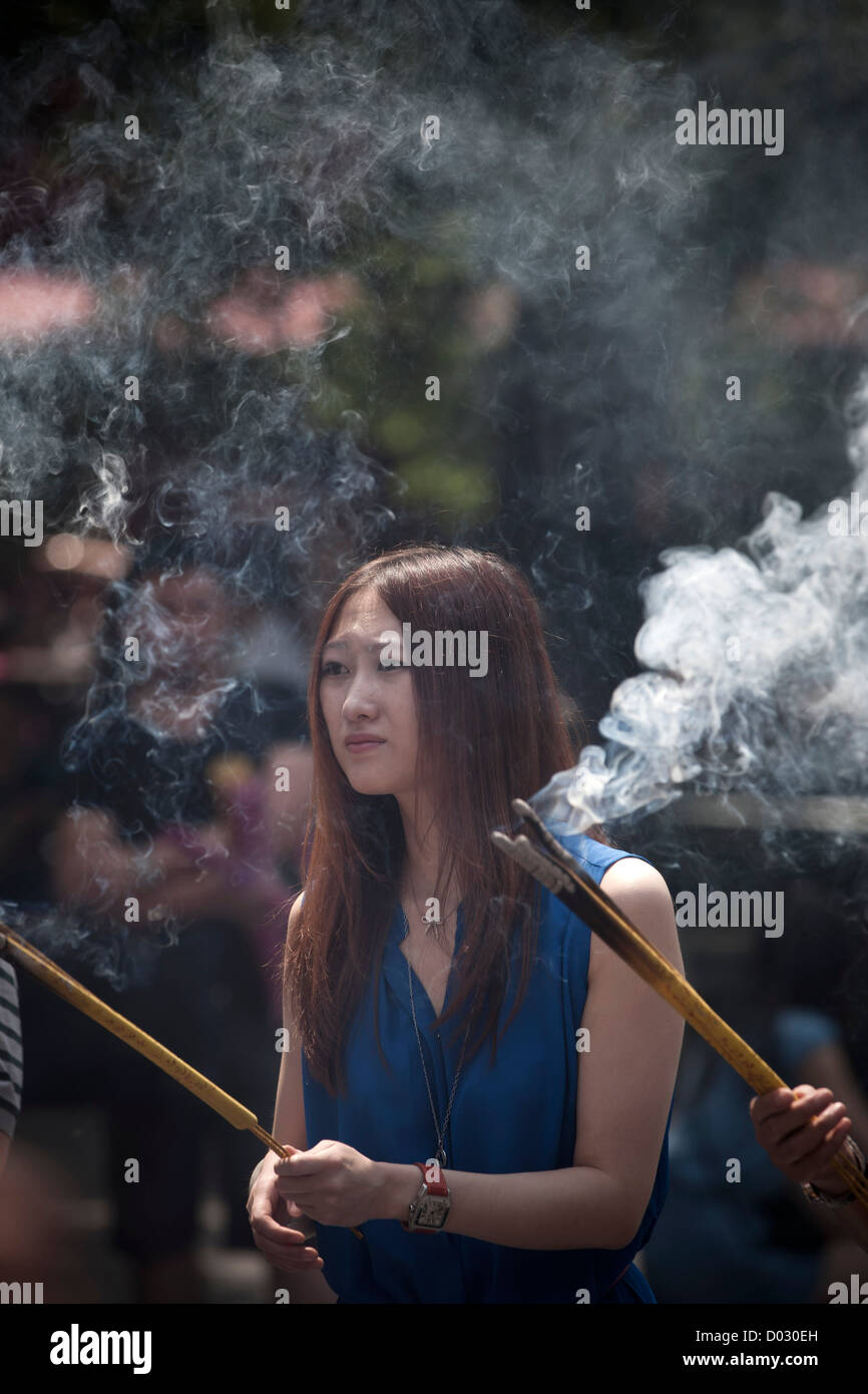 Una donna che brucia incenso prima di pregare presso le porte del tempio Lama a Pechino in Cina. Foto Stock