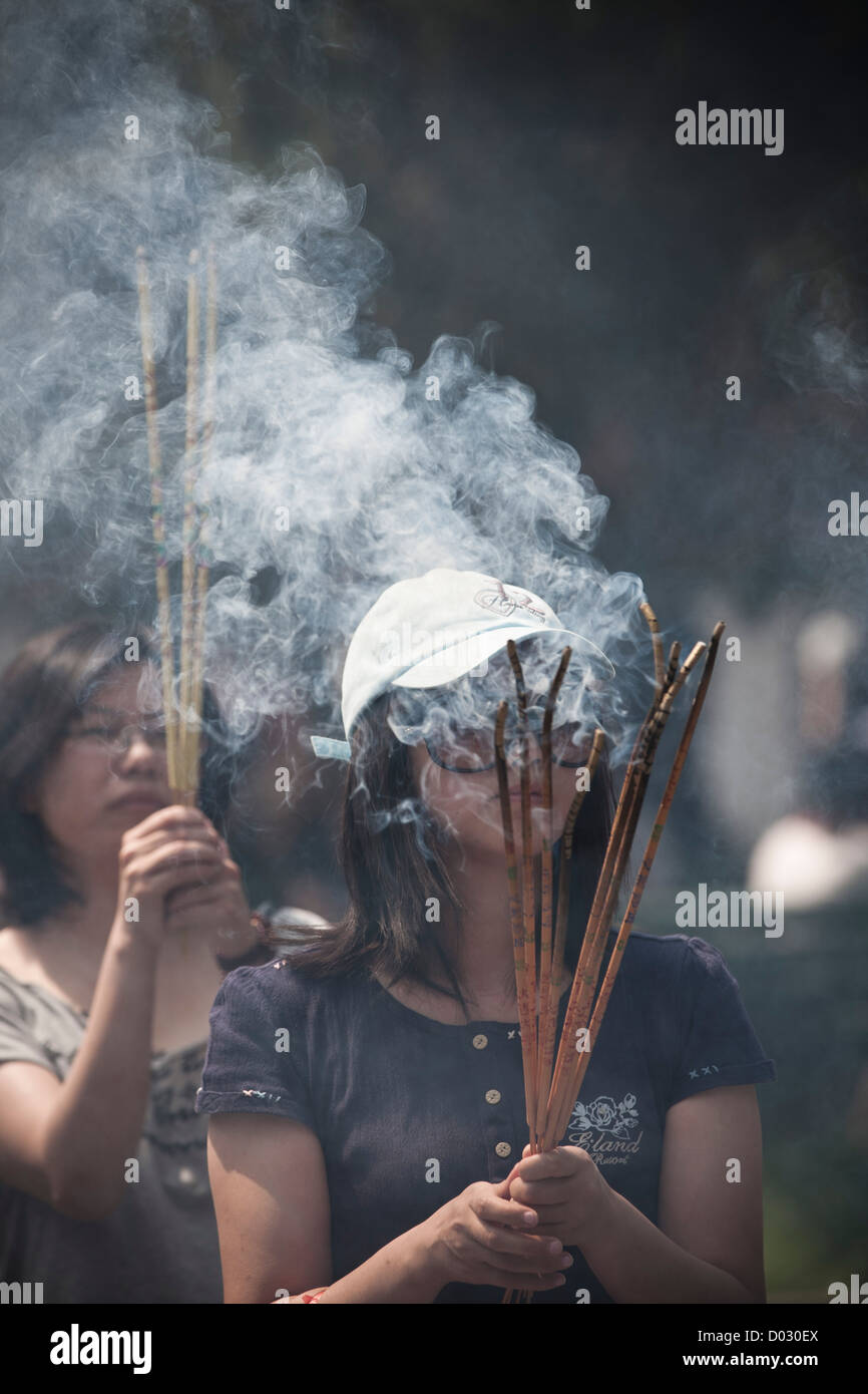 Una donna che brucia incenso prima di pregare presso le porte del tempio Lama a Pechino in Cina. Foto Stock