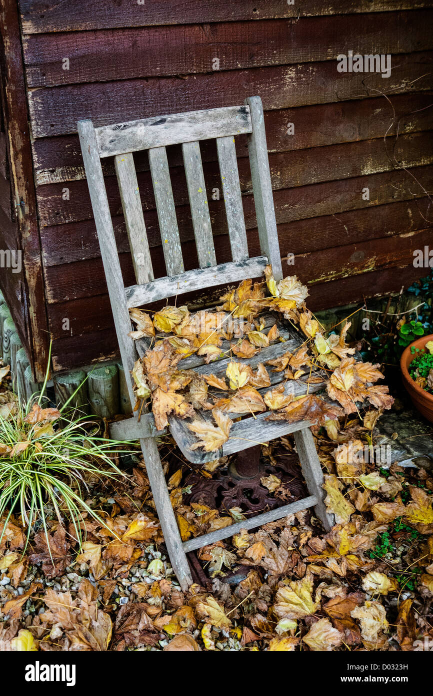 Una sedia da giardino bestrewn con foglie cadute in autunno / autunno Foto Stock