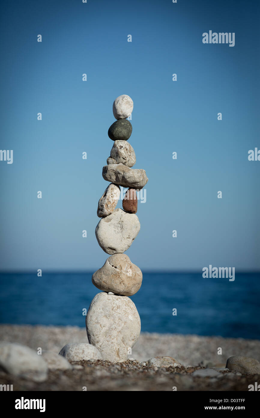 Pila di pietre di mare (ciottoli) in equilibrio su un mare e cielo sfondo Foto Stock