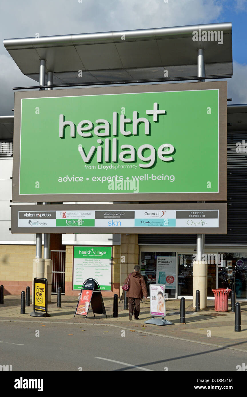 Donna shopper camminando verso la salute + Villaggio gestito da Lloyds farmacia che offre una gamma di servizi di assistenza sanitaria Foto Stock