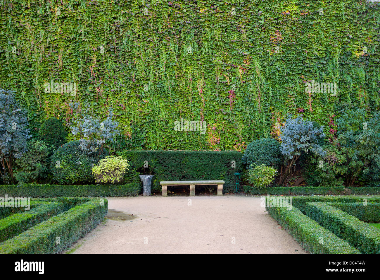 Una panchina nel parco lungo coperto di edera muro nel giardino del Hotel de Sully, Les Marais, Parigi Francia Foto Stock