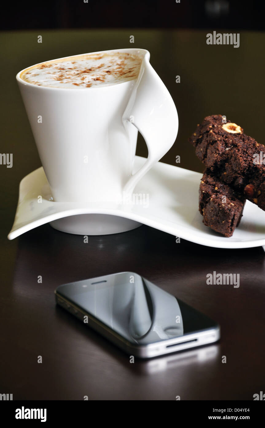 Caffè con spuma di cioccolato e nocciola biscottis in fantasia set di tazza e iPhone accanto a loro Foto Stock