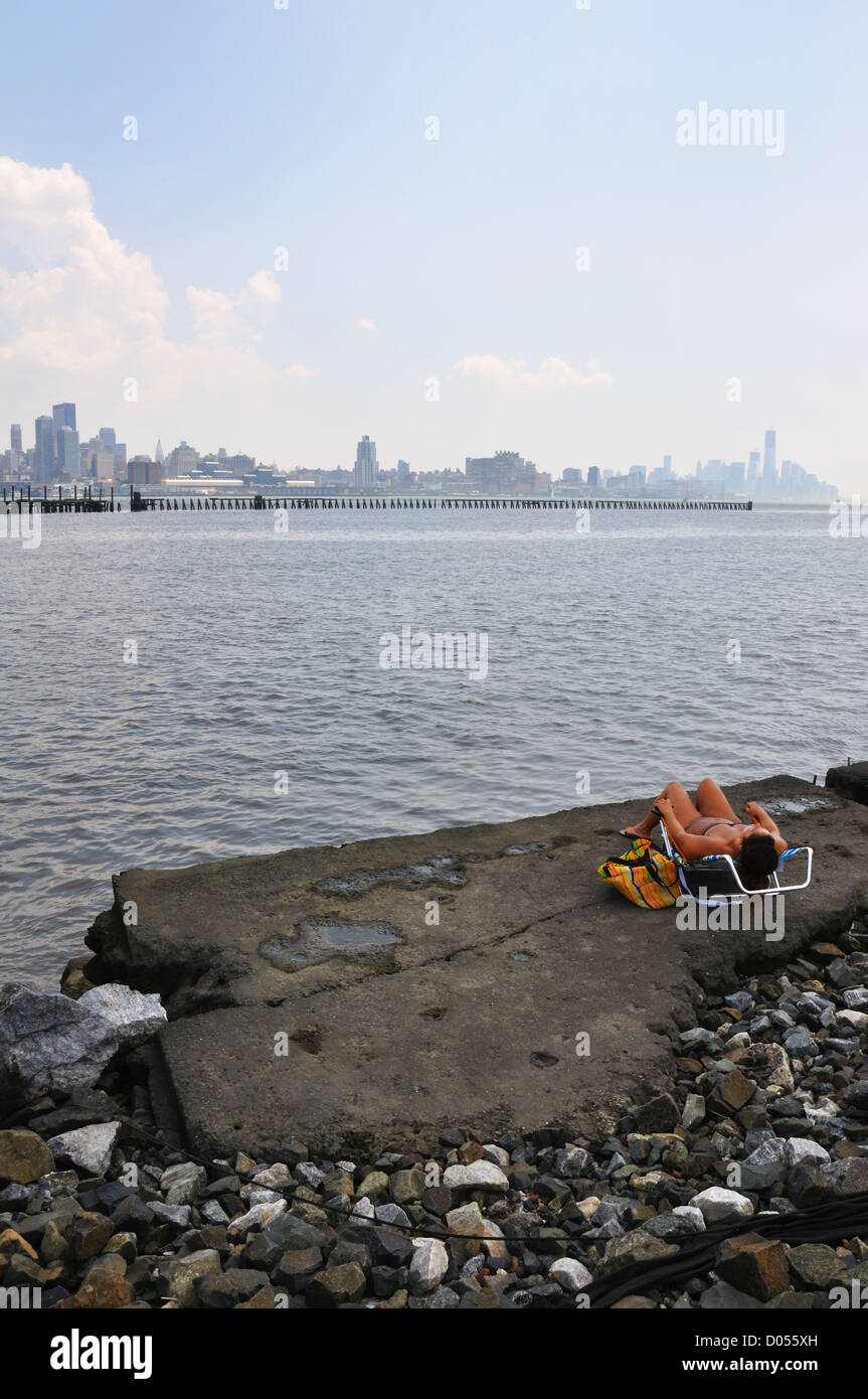 Vista di Manhattan a New York City, Stati Uniti d'America - si vede attraverso il Fiume Hudson da New Jersey - giovane donna a prendere il sole Foto Stock