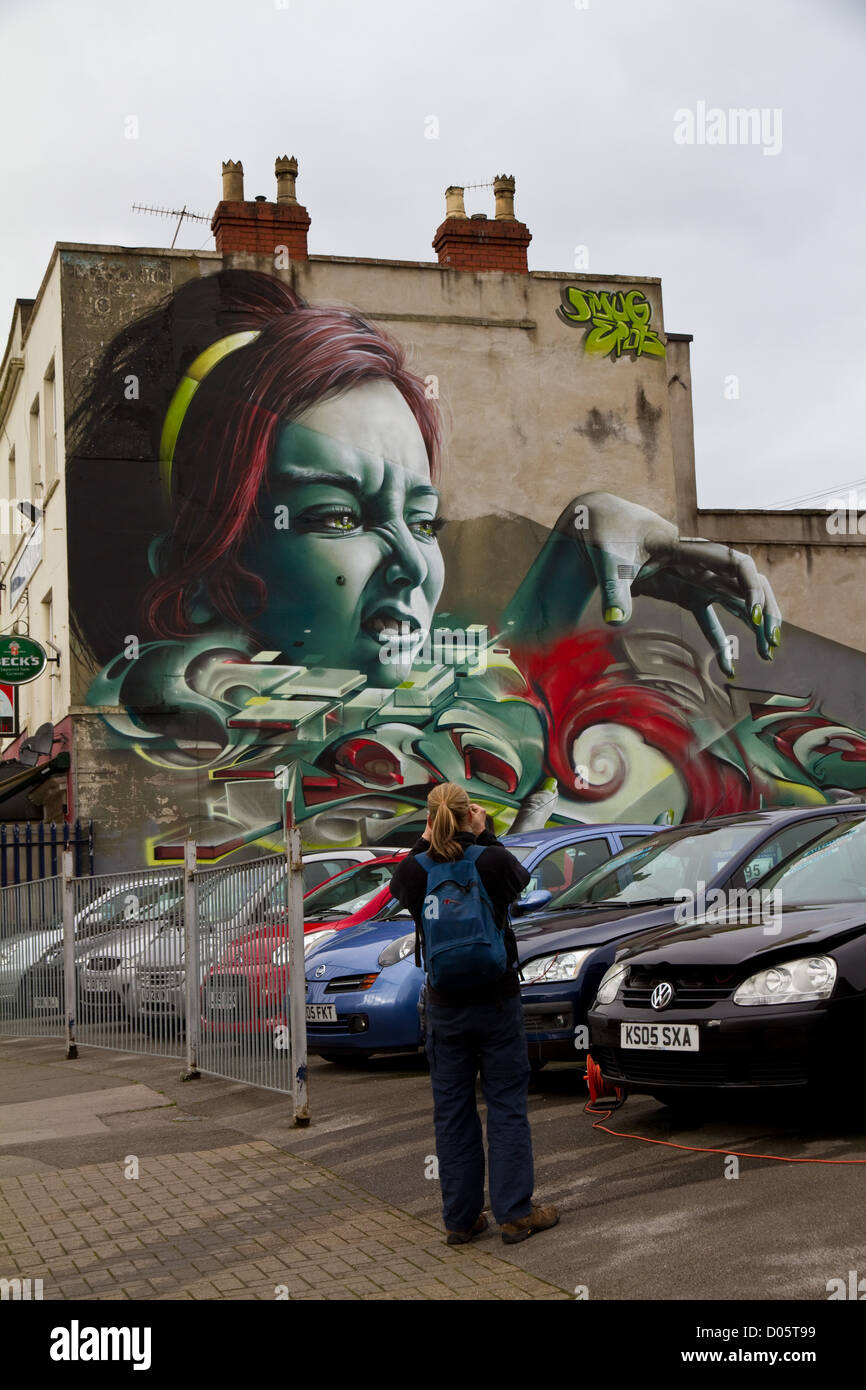 Graffiti di sneering uno volto di donna con prendendola per mano, occhi verdi e verde-dipinto le unghie al di sopra di un rivenditore di auto in Bristol Foto Stock