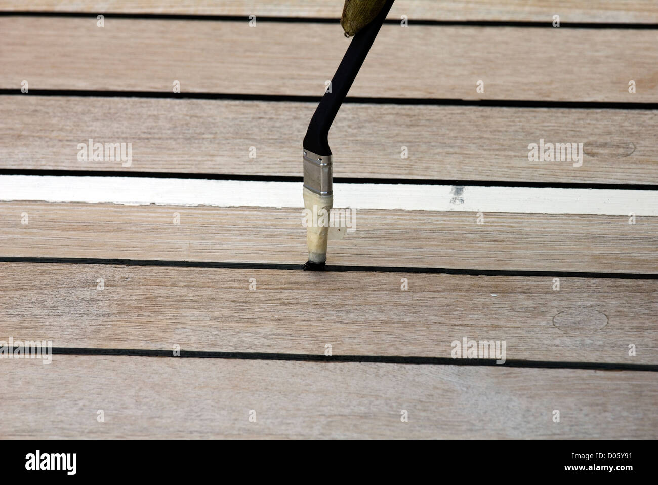 Verniciatura dei sigilli tra tavole di legno di teak nell'area shuffle board della Queen Mary 2. Ciò consente al puck di scivolare su di esso Foto Stock