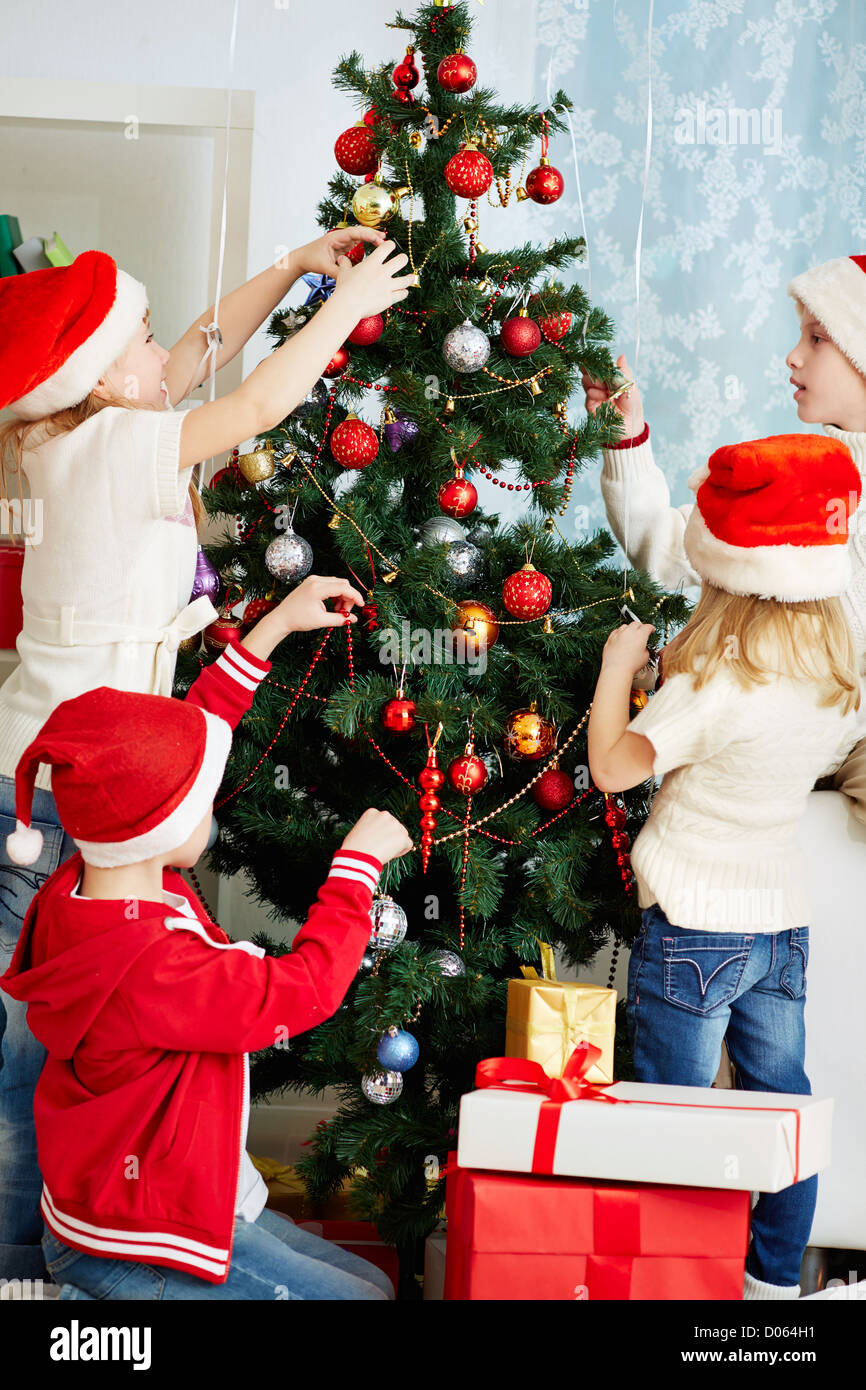 Un gruppo di ragazzi adorabili in Santa caps decorare albero di natale Foto Stock