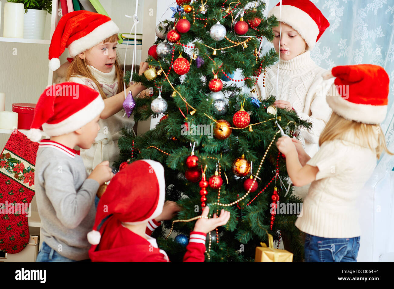 Un gruppo di ragazzi adorabili in Santa caps decorare albero di natale Foto Stock