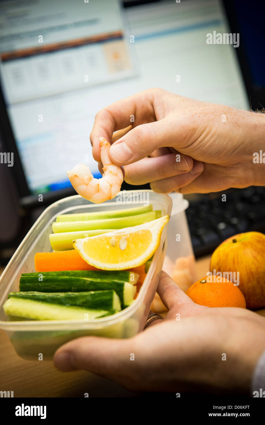 Un sano snack per il pranzo consumato mentre lavorano ad una scrivania. Il monitoraggio in background. Foto Stock