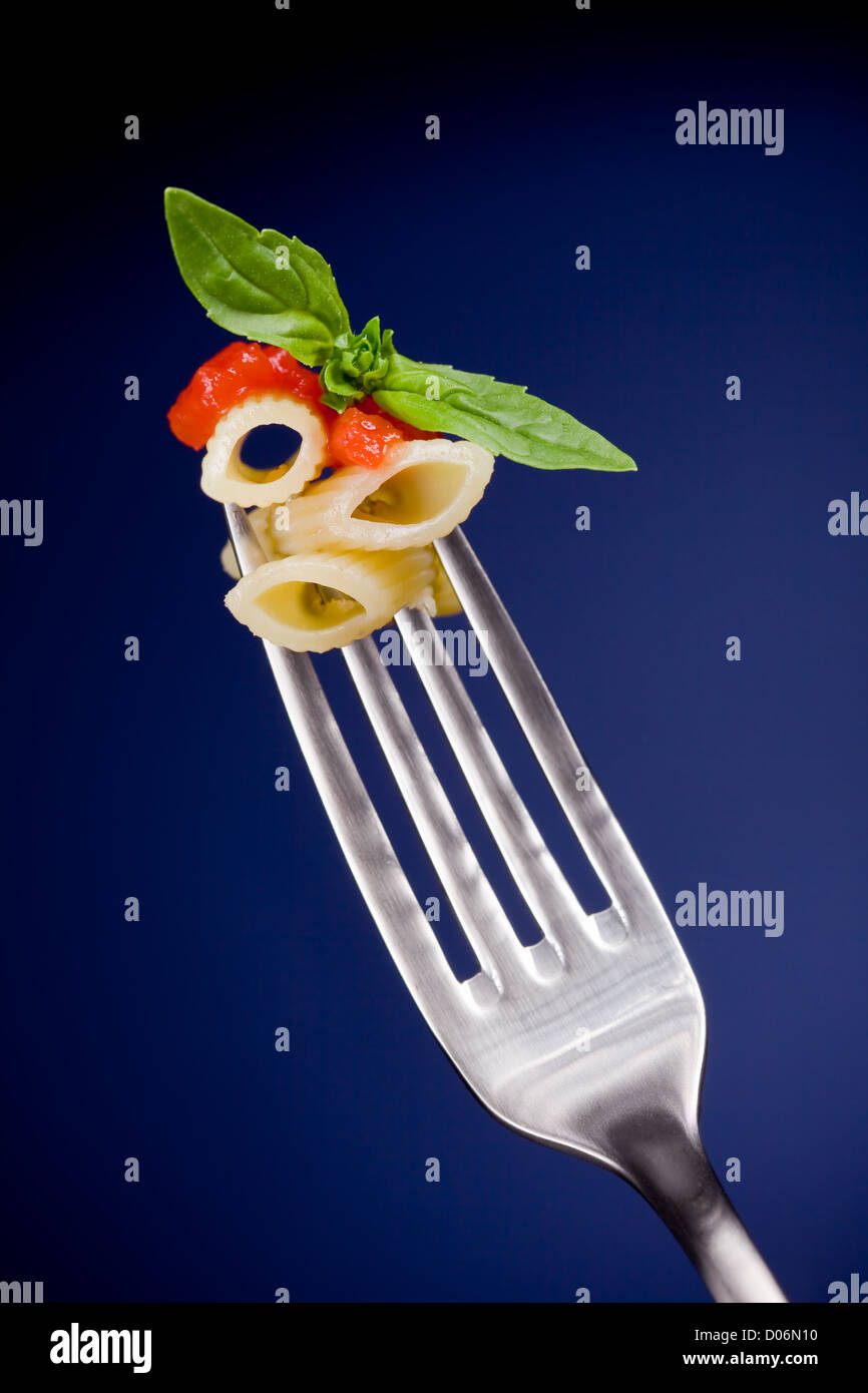 Deliziosi piatti di pasta italiana con salsa di pomodoro e basilico sulla forcella su sfondo blu Foto Stock