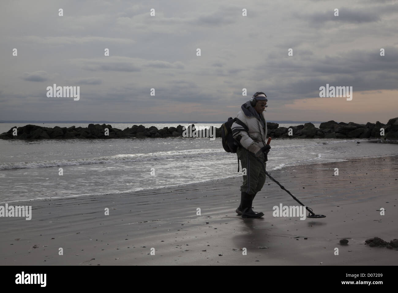 L'uomo pettini spiaggia a Coney Island con un rivelatore di metalli nella speranza che il ciclone Sandy ha scoperto alcuni tesori sepolti. Foto Stock