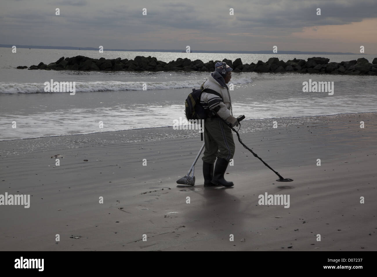 L'uomo pettini spiaggia a Coney Island con un rivelatore di metalli nella speranza che il ciclone Sandy ha scoperto alcuni tesori sepolti. Foto Stock