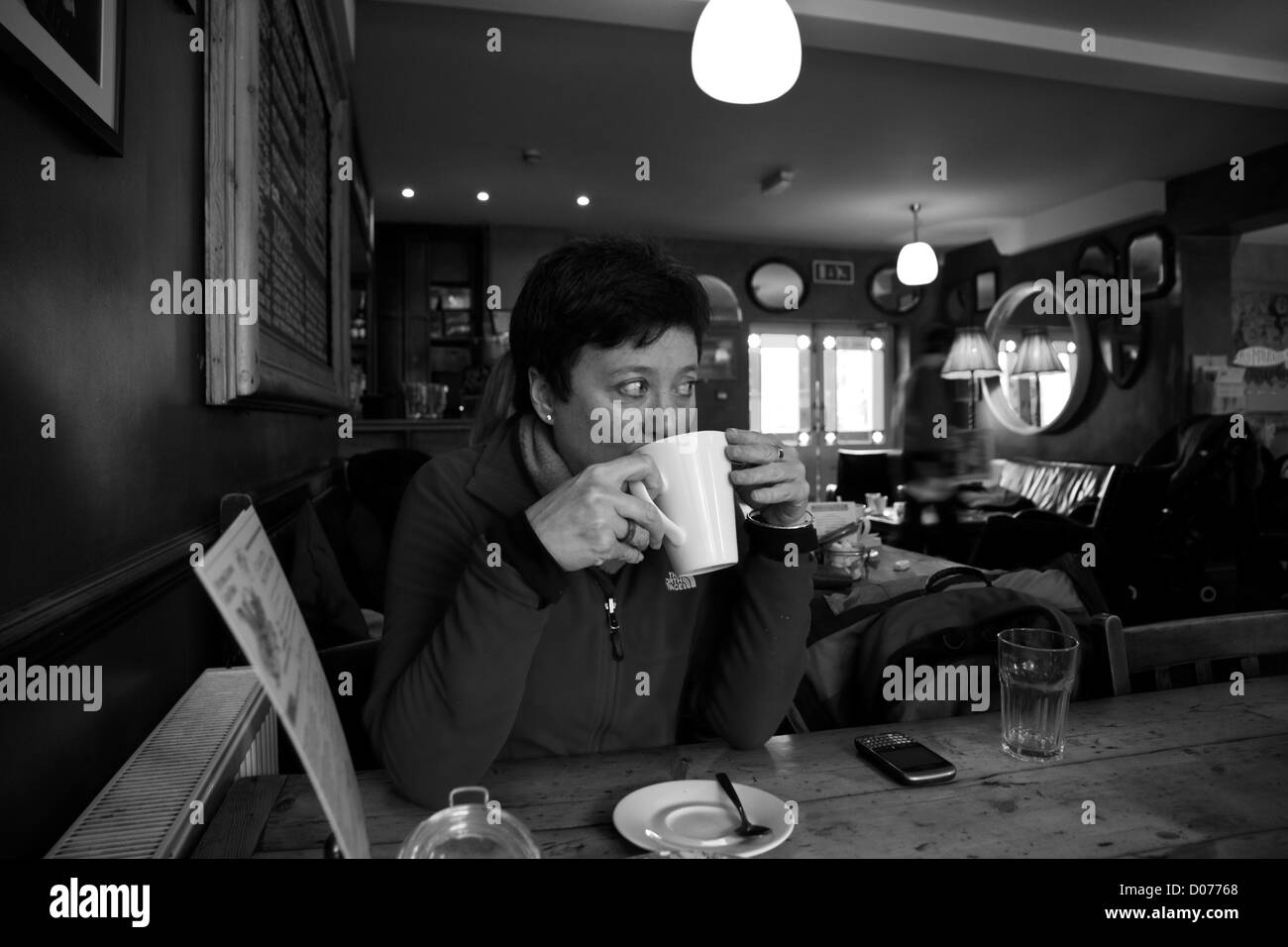 Una donna che beve caffè in un bar/caffè Foto Stock