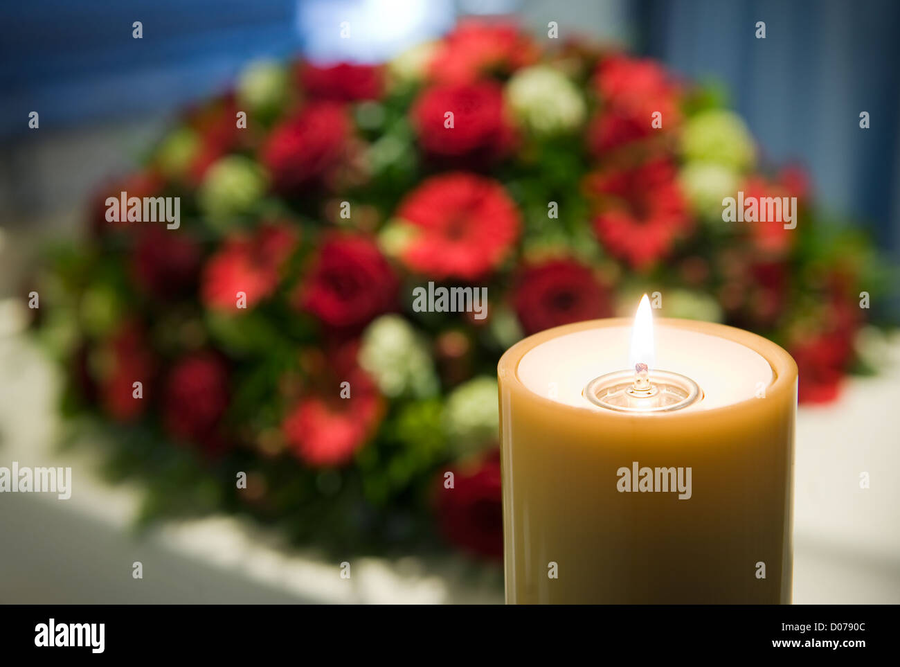 Una candela che brucia con una bara di bianco e un omaggio floreale sullo sfondo in una camera mortuaria Foto Stock