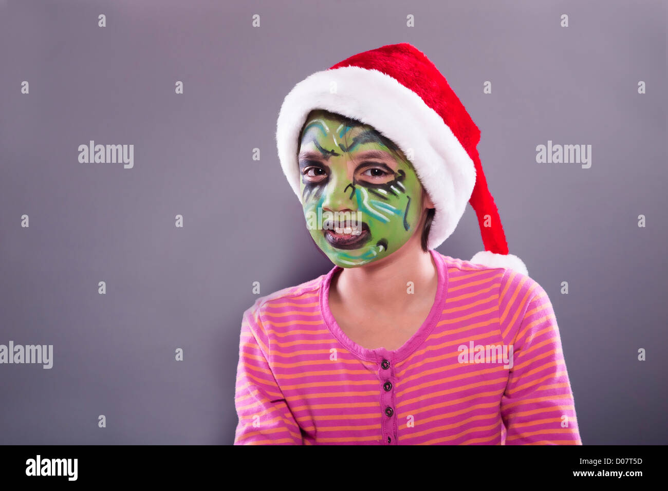 Una bambina indossa un cappello da Babbo Natale e ha volto la vernice simile a il Grinch. Foto Stock