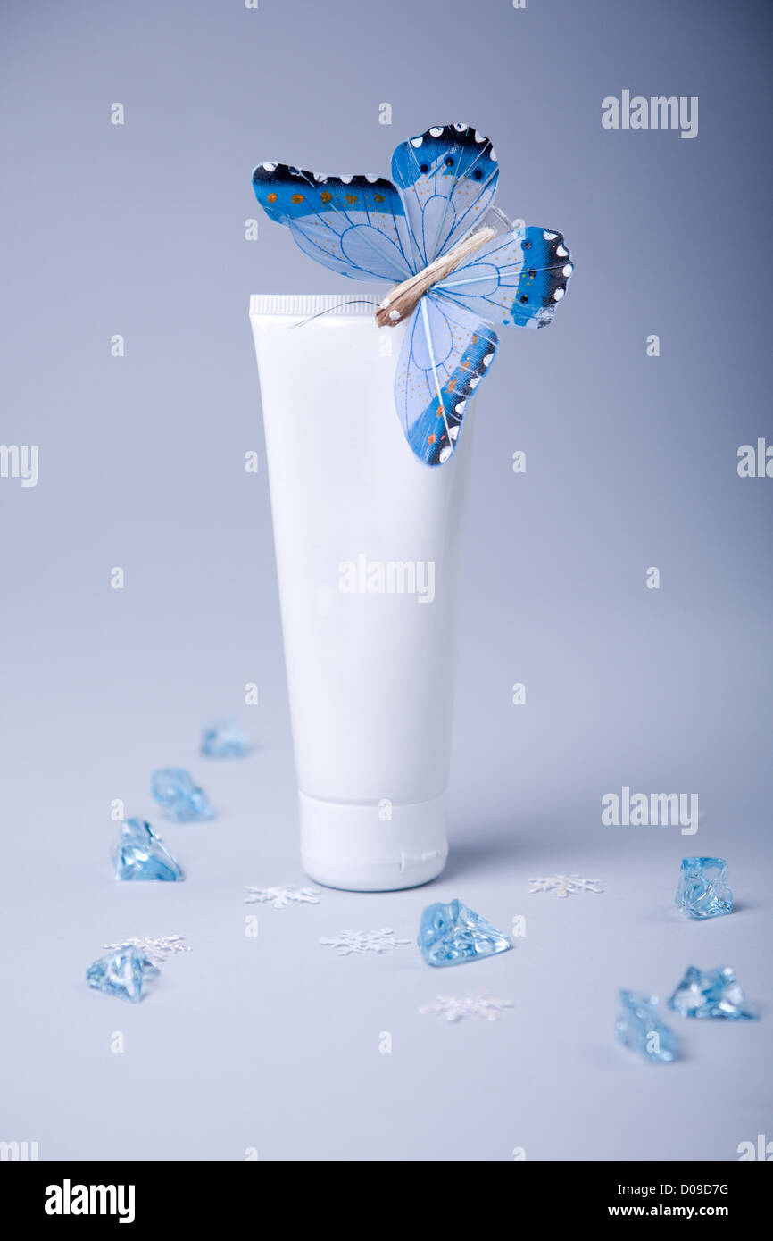 Bianco tubo cosmetico con la zona vuota con blue butterfly su blu-grigio tra i cristalli blu Foto Stock