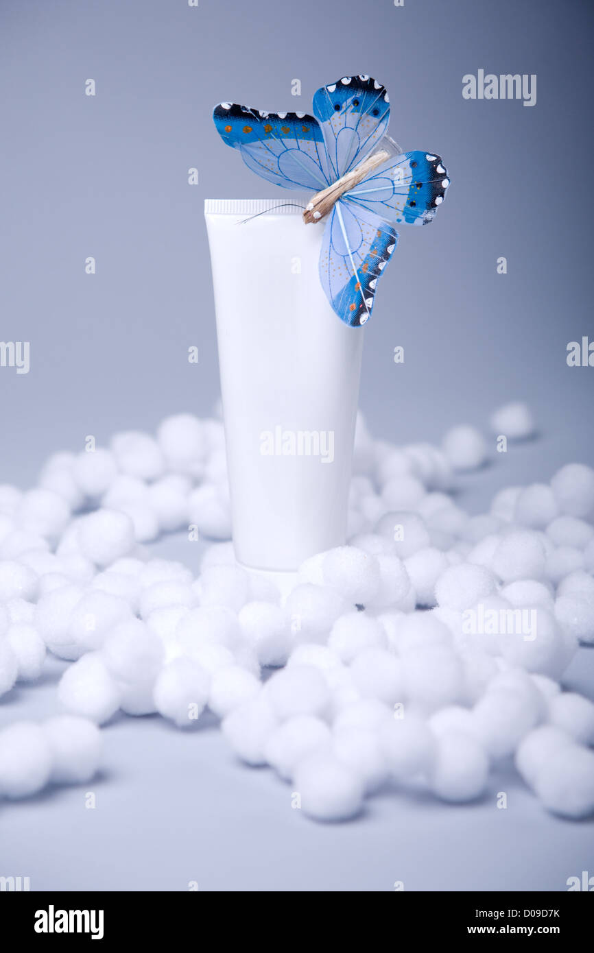Bianco tubo cosmetico con la zona vuota con blue butterfly su blu-grigio Sfondo nella neve artificiale Foto Stock