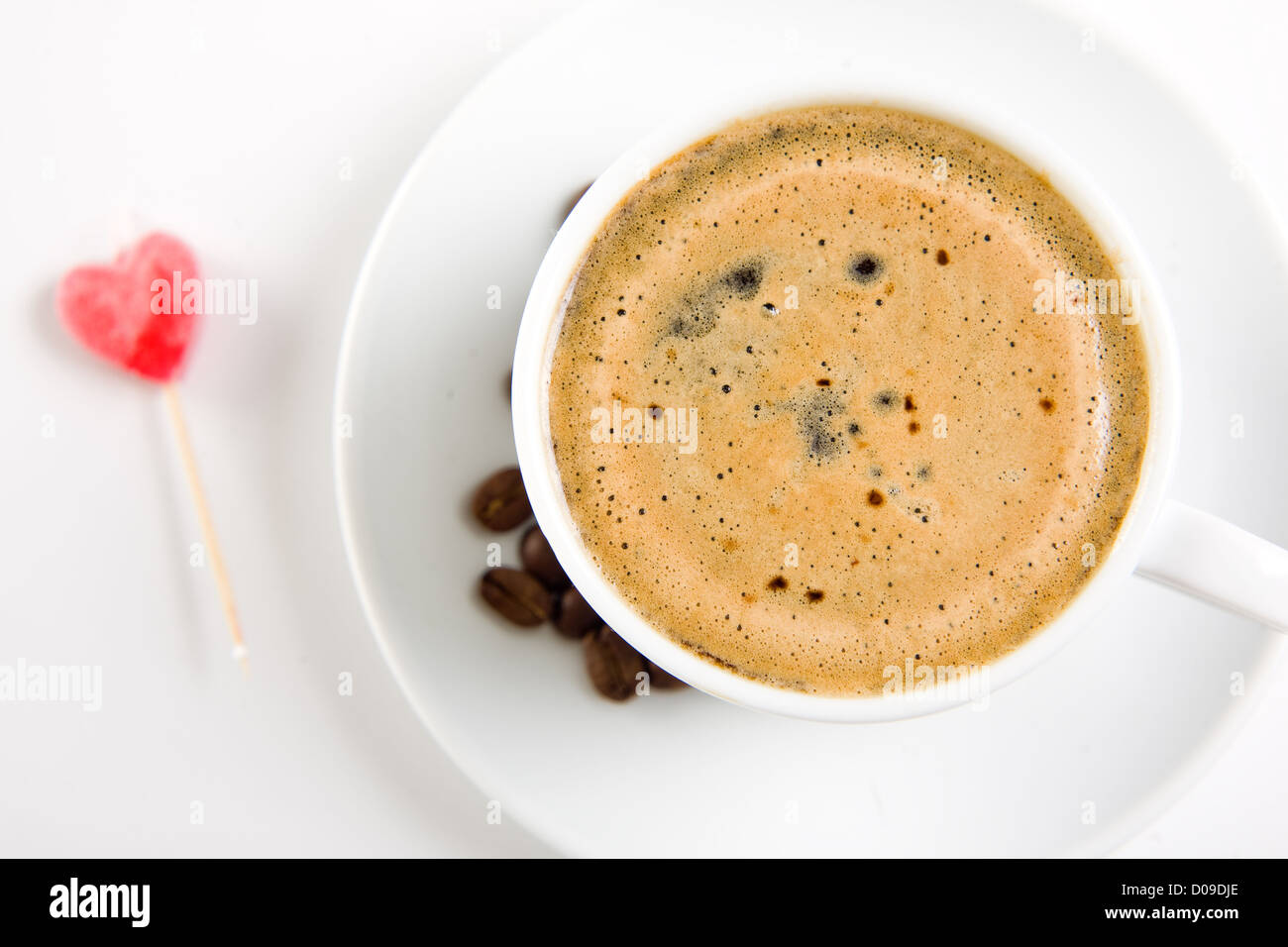 Tazza di caffè su bianco con la caramella cuore su sfondo, concentrarsi sul liquido Foto Stock