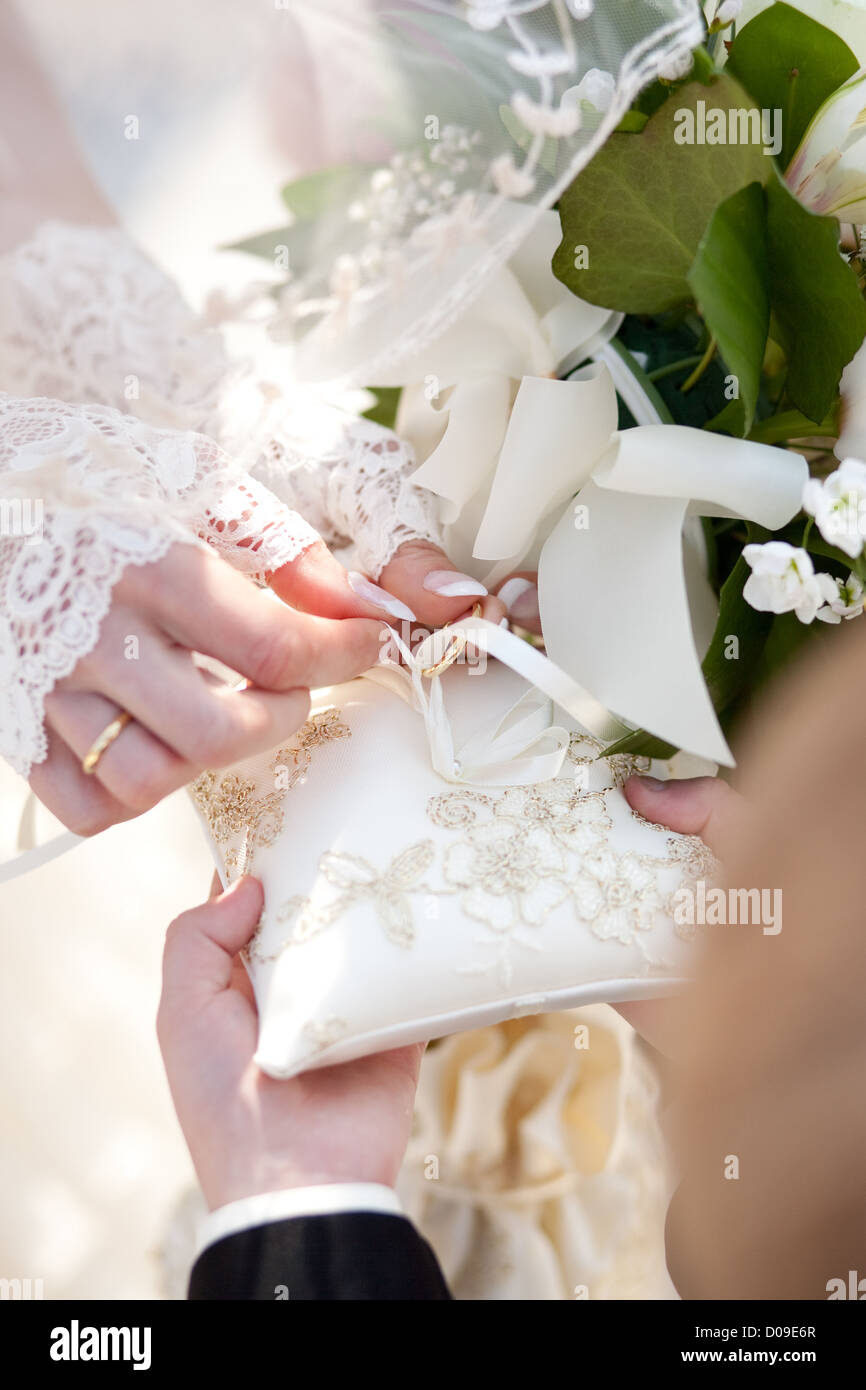 Sposa tenendo anello dal cuscino di seta alla cerimonia di nozze Foto Stock