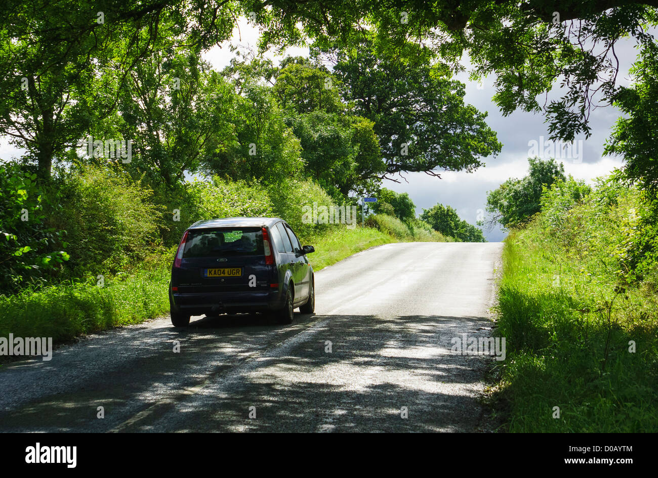 Una guida auto fino alla cima di una collina su un vicolo del paese attraverso gli alberi in una giornata di sole. Foto Stock