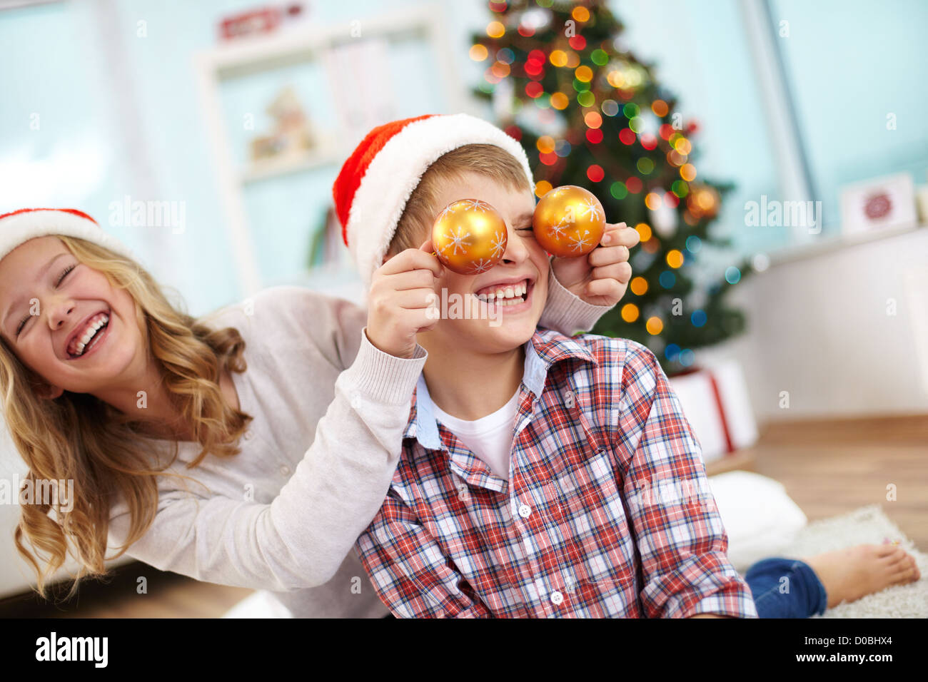Ritratto di felice ragazza con decorativi sfere giocattolo da suo fratello negli occhi e entrambi a ridere della sera di Natale Foto Stock