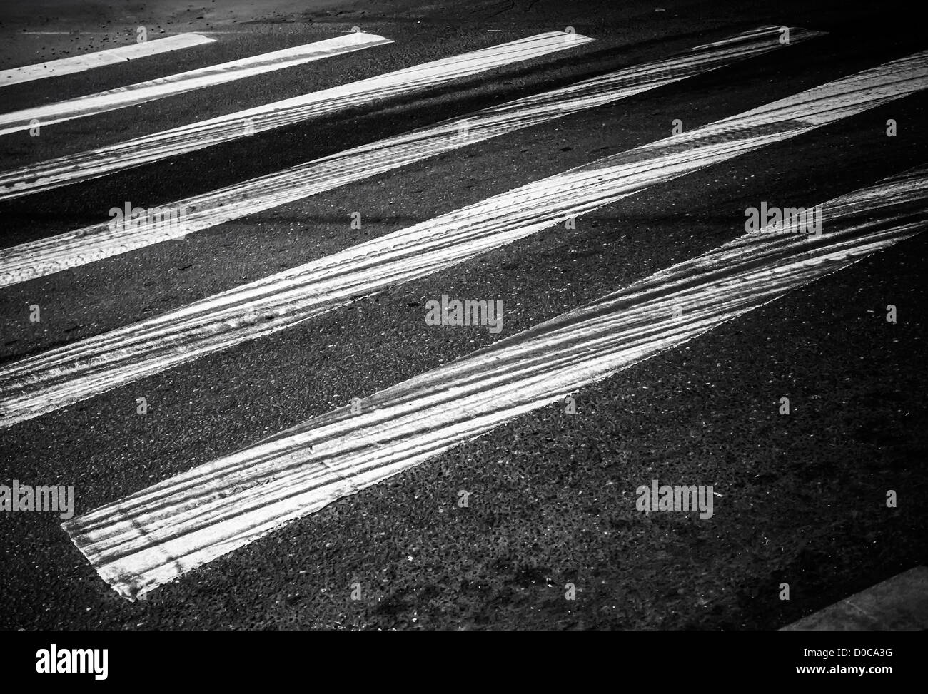 Pericolo attraversamento pedonale con rettangoli bianchi e piste di frenatura sul buio asfalto Foto Stock