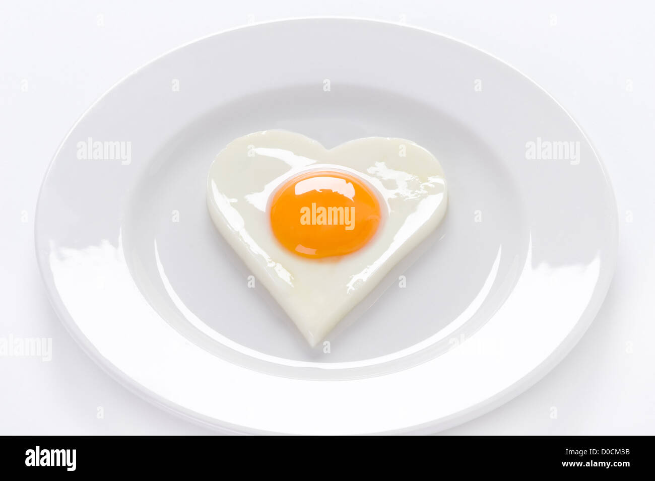 A forma di cuore uovo cotto presentato soft 'sunny lato verso l'alto' su una circolare bianco piastra sagomata su sfondo bianco Foto Stock