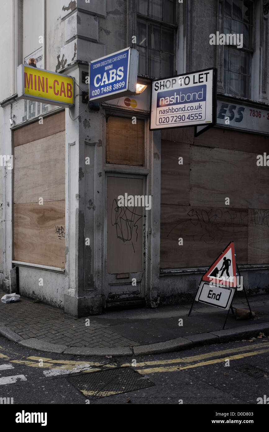 Un saliti fino al centro di Londra mini cab business e un fine di opere segno a triangolo su un angolo di Holborn. Il visual pun gioca fuori del segno triangolare che ci dice che il lavoro ha terminato un messaggio comprendiamo anche dall'plyboard attaccata alla ex locali commerciali, fissandolo da vandali, squatter o occupazione illegale. Una luce di sicurezza burns 24/7 e la vecchia cabina ufficio dettagli dell'insieme con la proprietà agente. Foto Stock