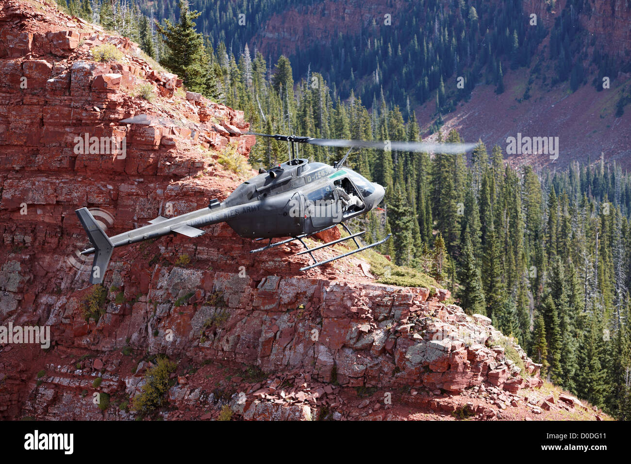 Una campana OH-58 Kiowa aleggia appena al di sopra di una ripida scogliera alta in Colorado di montagne rocciose. Foto Stock