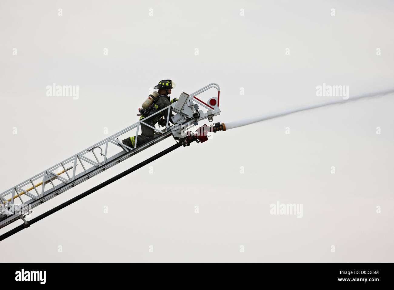 Firefighter spruzzare acqua sul fuoco edificio dalla fine di una scaletta, utilizzando un cannone ad acqua. Foto Stock