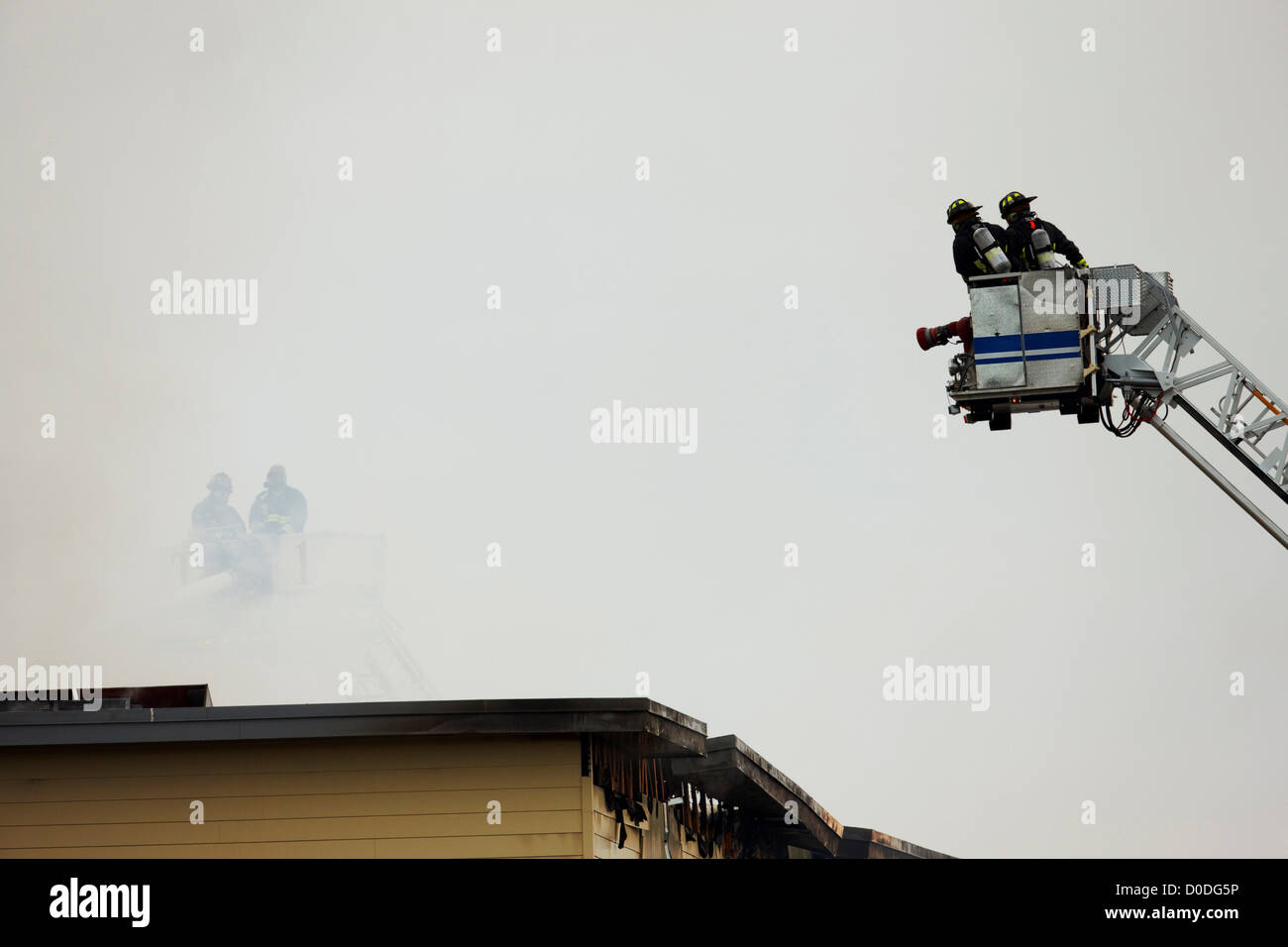 Vigili del fuoco sopra il fuoco e l acqua danneggiato il tetto di un edificio, all'interno di un cestello alla fine di una scala della torre. Foto Stock
