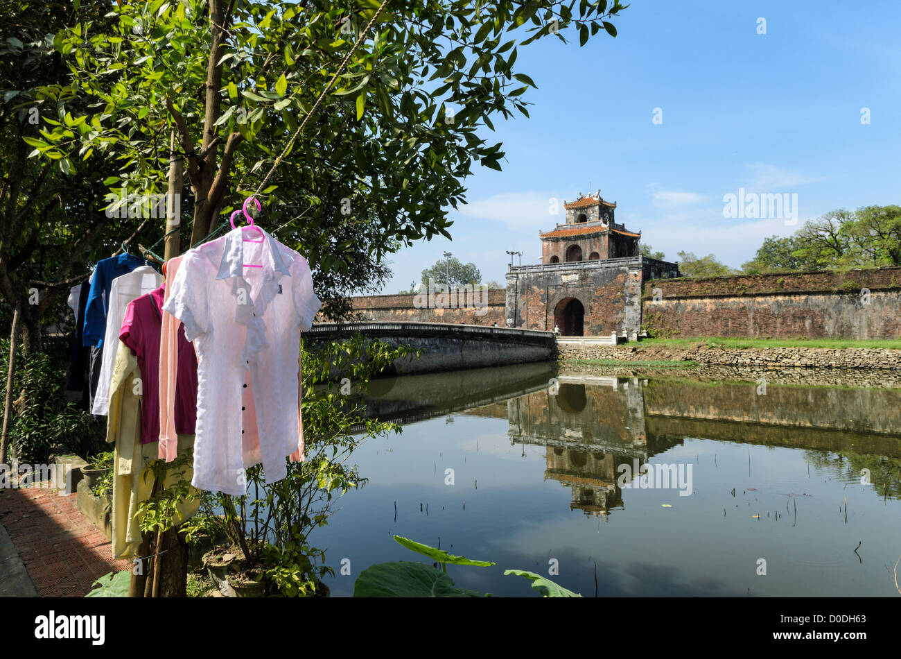 Imperial City Moat Laundry Hue Vietnam // HUE, Vietnam - i residenti locali dall'altra parte del fossato passano il bucato per asciugare presso la città imperiale di Hue, Vietnam. Un palazzo auto-chiuso e fortificato, il complesso comprende la città Proibita viola, che era il santuario interno della casa imperiale, nonché templi, cortili, giardini e altri edifici. Gran parte della città imperiale fu danneggiata o distrutta durante la guerra del Vietnam. È ora dichiarato patrimonio dell'umanità dell'UNESCO. Foto Stock
