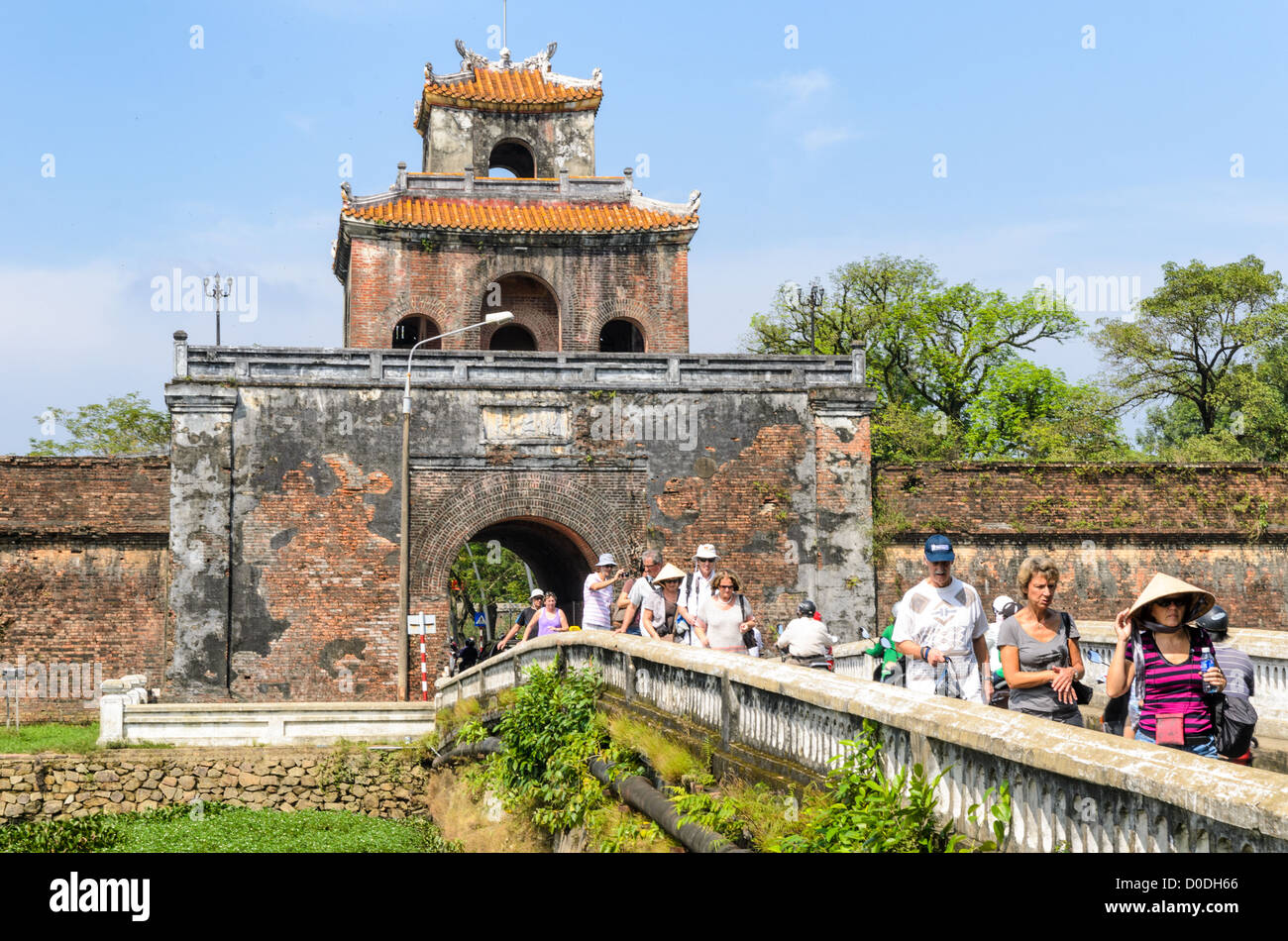 HUE, Vietnam - i turisti a piedi attraverso un ponte sopra il fossato da una torre di guardia alla città imperiale di Hue, Vietnam. Un auto-racchiuso e palazzo fortificato, il complesso comprende il viola la Città Proibita, che era il sanctum interno della casa imperiale, così come i templi, cortili, giardini, e altri edifici. Gran parte della città imperiale è stato danneggiato o distrutto durante la Guerra del Vietnam. È ora indicato come sito del Patrimonio Mondiale dell'UNESCO. Foto Stock