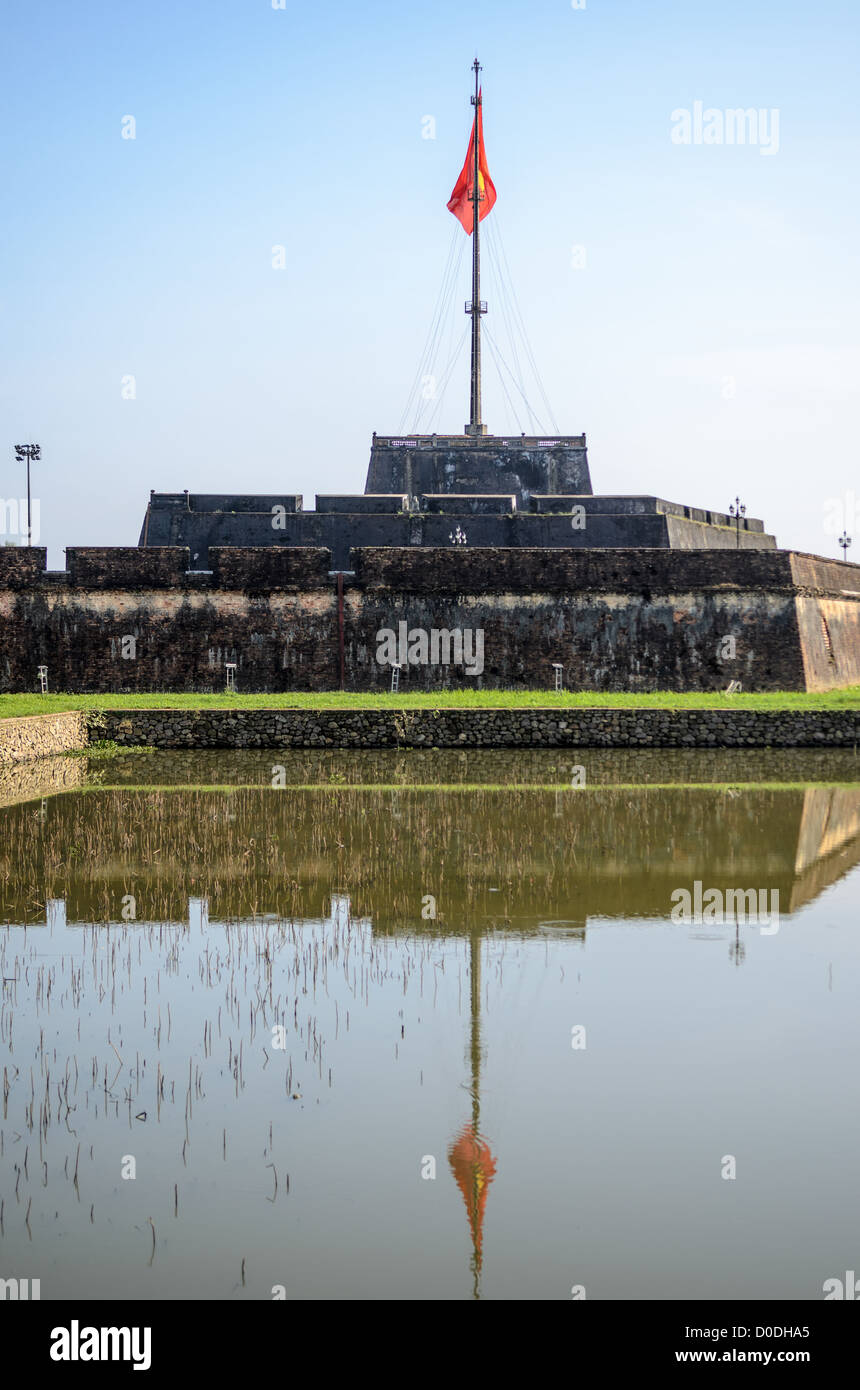 Imperial City Vietnamita Flag Reflection Hue Vietnam // HUE, Vietnam — la grande bandiera vietnamita alla cittadella si riflette sul fossato difensivo della città imperiale di Hue, Vietnam. Un palazzo auto-chiuso e fortificato, il complesso comprende la città Proibita viola, che era il santuario interno della casa imperiale, nonché templi, cortili, giardini e altri edifici. Gran parte della città imperiale fu danneggiata o distrutta durante la guerra del Vietnam. È ora dichiarato patrimonio dell'umanità dell'UNESCO. Foto Stock