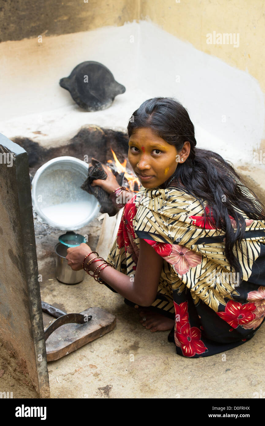 Sud giovane donna indiana di latte bollente su un fuoco aperto nel suo villaggio rurale home. Andhra Pradesh, India Foto Stock