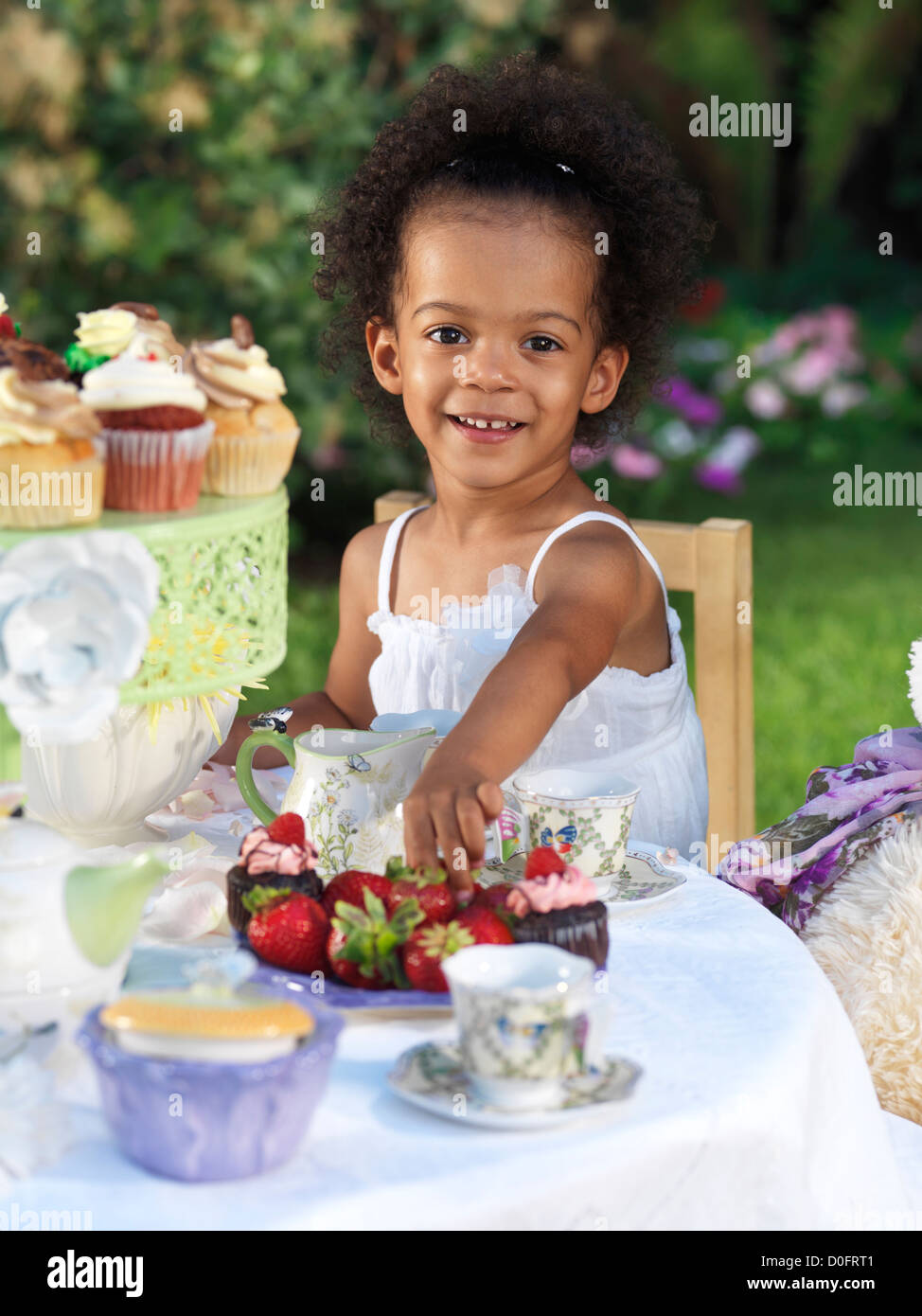 Licenza disponibile a MaximImages.com - ragazza sorridente felice che ha una festa estiva all'aperto. Bere tè con cupcake. Foto Stock