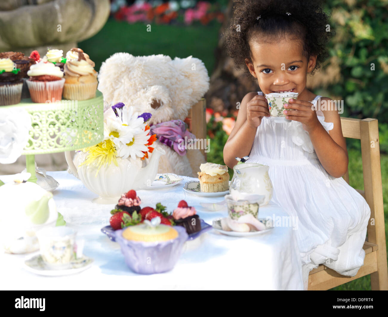 Licenza disponibile a MaximImages.com - ragazza sorridente felice che ha una festa estiva all'aperto. Bere tè con cupcake. Foto Stock