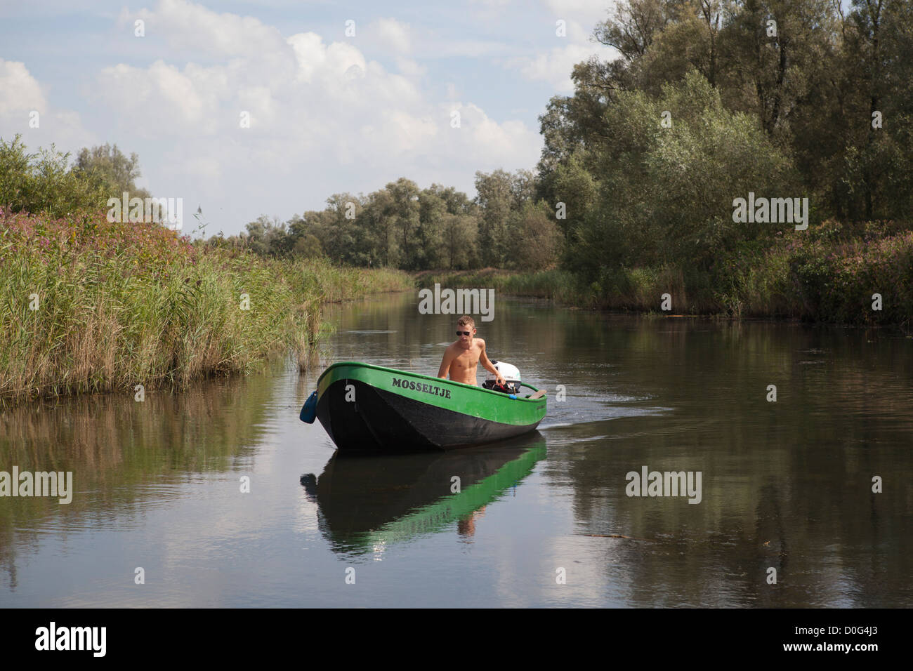 Giovane uomo in un piccolo motoscafo passando il fiume nel Parco Nazionale il Biesbosch su una calda giornata nei Paesi Bassi Foto Stock
