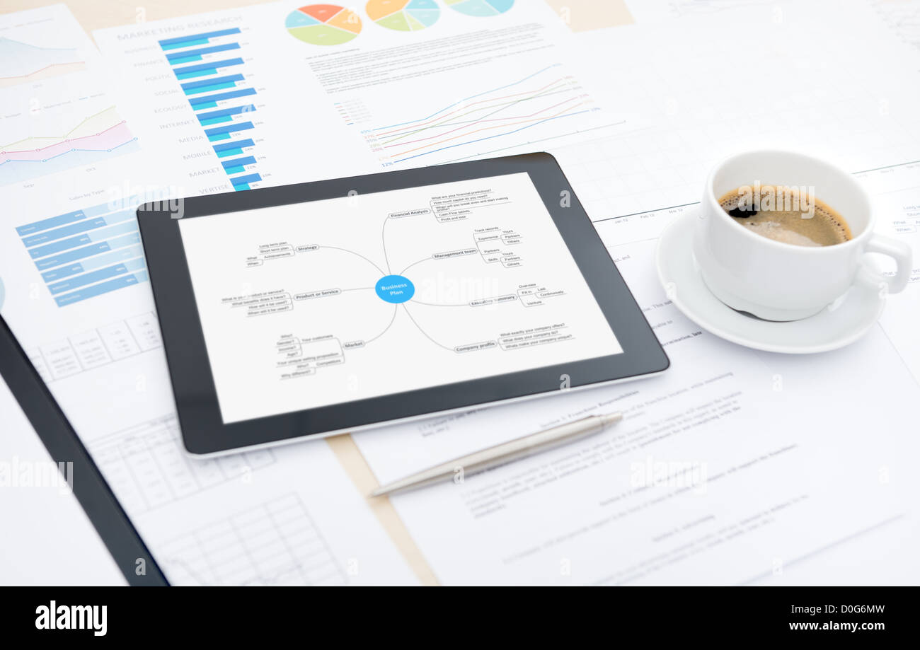 Moderna tavoletta digitale con il business plan sullo schermo, una tazza di caffè e alcune carte su una scrivania in ufficio. Foto Stock