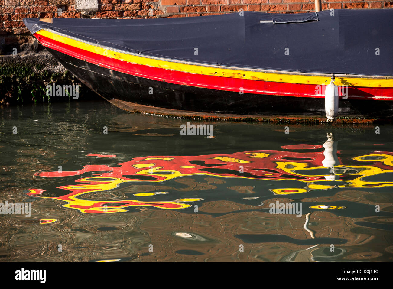 Dettaglio della prua di una piccola barca verniciato nei colori della bandiera tedesca e il suo riflesso distorto in acqua increspata Foto Stock