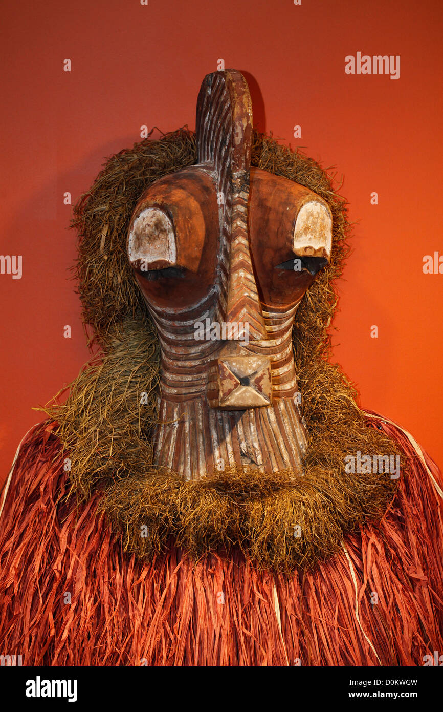 Una maschera africana, del popolo Yaka o Songye della Repubblica Democratica del Congo.in Africa caratterizzata dal suo viso allungato e intagliato in legno e da un grande copricapo in fibre vegetali, che sembra essere la rafia Foto Stock