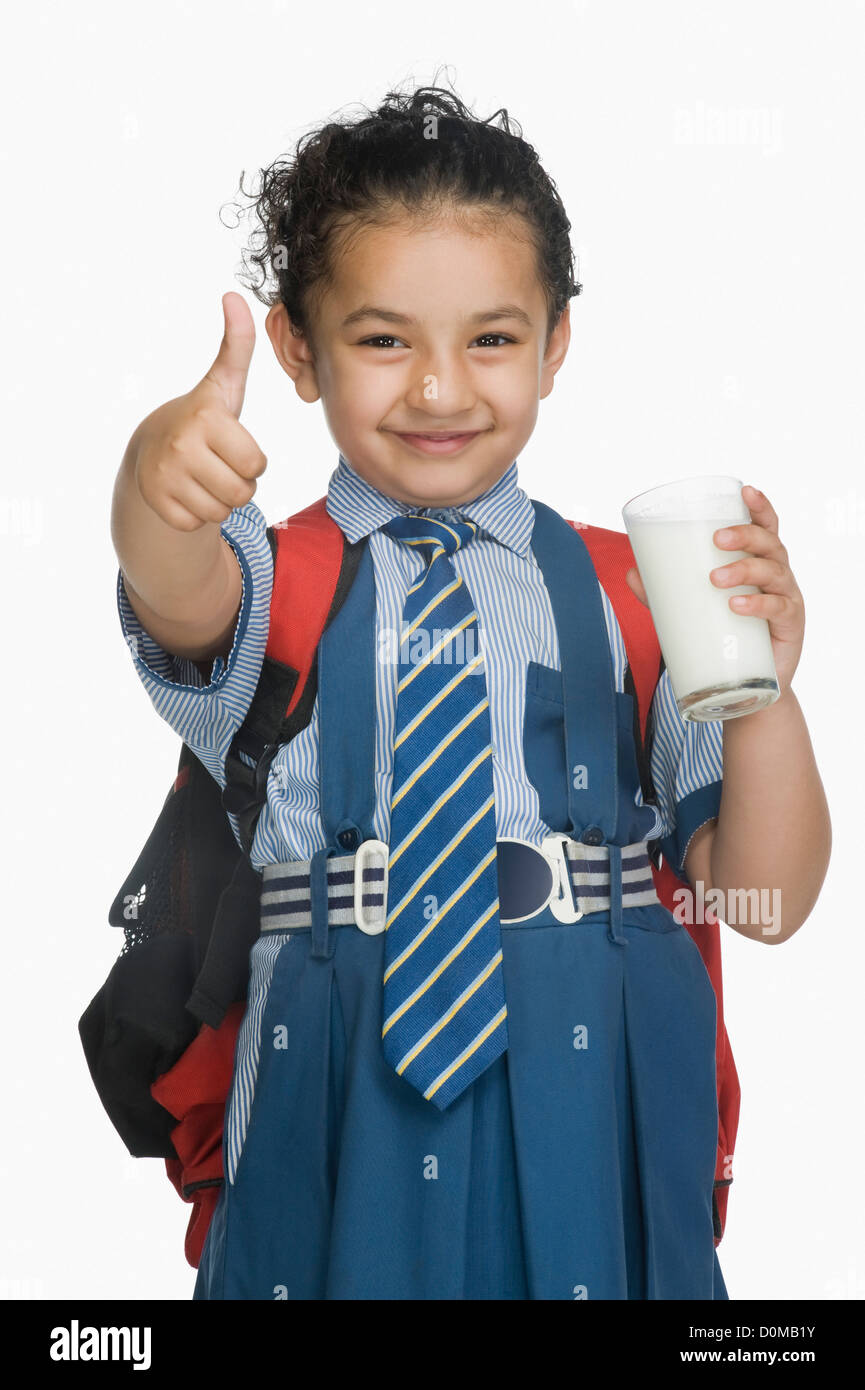Schoolgirl tenendo un bicchiere di latte e mostrando pollice in alto segno Foto Stock
