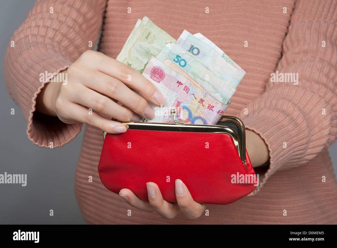 Donna cinese Yuan di contenimento di banconote la moneta ufficiale della Cina continentale con un portamonete rosso Foto Stock