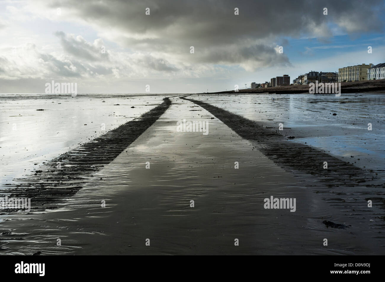 Le tracce delle ruote su una spiaggia bagnata che conduce all'orizzonte Foto Stock