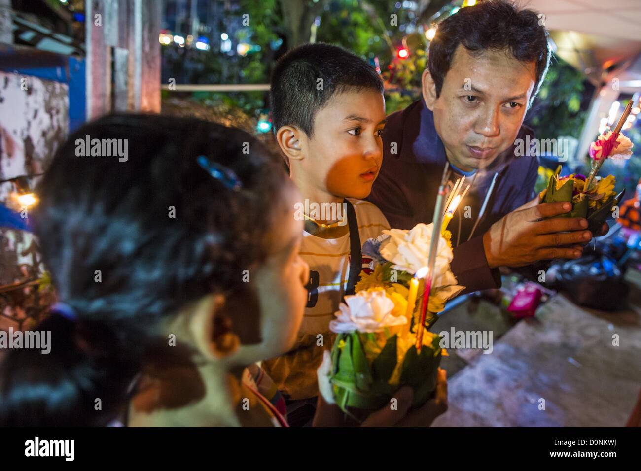 Nov. 28, 2012 - Bangkok, Tailandia - un uomo parla ai suoi figli circa il Loy Krathong traditon al Wat Yannawa in Bangkok. Loy Krathong ha luogo la sera della luna piena del dodicesimo mese in tailandese tradizionale calendario lunare. Nel calendario occidentale questo di solito cade nel mese di novembre. Loy significa 'flottante', mentre krathong si riferisce al solito lotus-contenitore sagomato che galleggia sull'acqua. Krathongs tradizionali sono fatti di strati del tronco di un albero di banana o uno spider lily impianto. Oggi molte persone utilizzano krathongs di pasta di pane cotto al forno che si disintegra nell'acqua e nutrire i pesci. Un Foto Stock